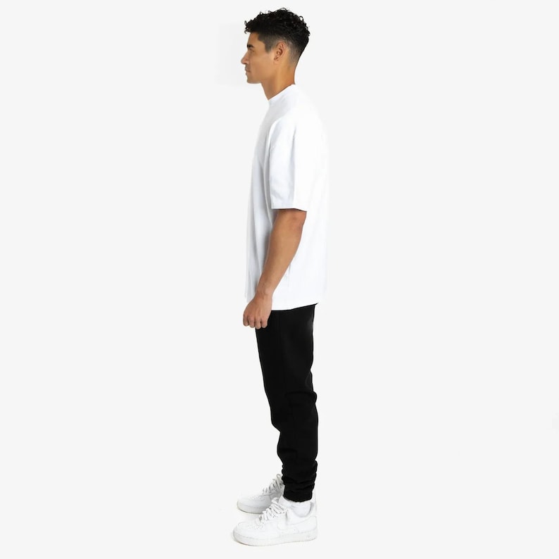 Puede incluir: Una persona vestida con una camiseta blanca de manga corta y pantalones negros. La persona tambi&eacute;n lleva zapatillas blancas. La camiseta tiene cuello redondo. Los pantalones son de color negro s&oacute;lido.