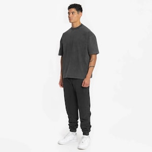 May include: A black oversized t-shirt with a crew neck and a pair of black sweatpants. The person is wearing white sneakers.