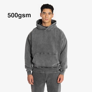 Puede incluir: Una sudadera con capucha gris con un bolsillo canguro. La sudadera está hecha de una tela gruesa de 500 g/m².
