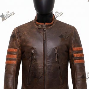 May include: A brown leather jacket with a stand-up collar and a zipper closure. The jacket has two vertical zippered pockets and brown stripes on the sleeves. The text "THE leather home SHOP" is visible on the jacket.