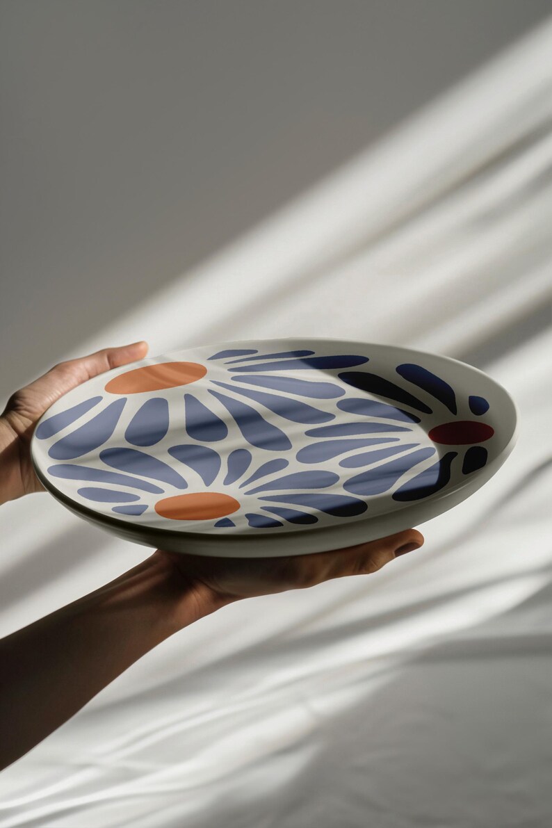 May include: A white ceramic serving platter with a blue and orange floral design. The platter is being held by a hand.