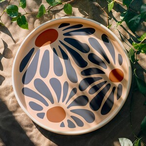 May include: A round tray with a cream background and a floral design. The flowers are blue and black with orange centers.