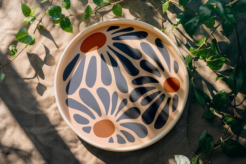 May include: A round tray with a cream background and a floral design. The flowers are blue and black with orange centers.
