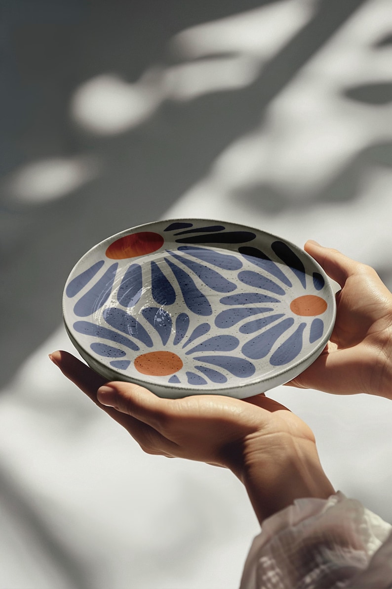 May include: A white ceramic bowl with a blue and orange floral design. The bowl is being held by a person's hands.