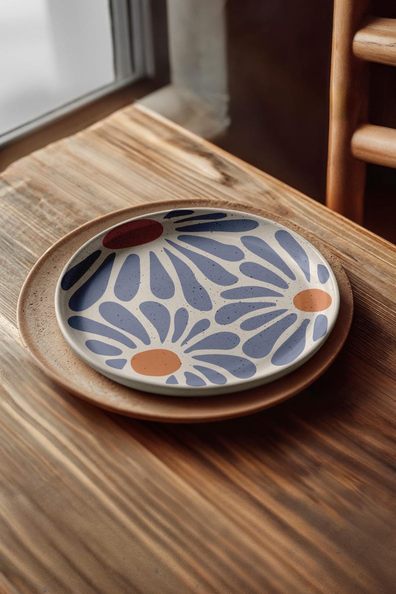 May include: A white ceramic plate with a blue and orange floral pattern. The plate is on a wooden table.