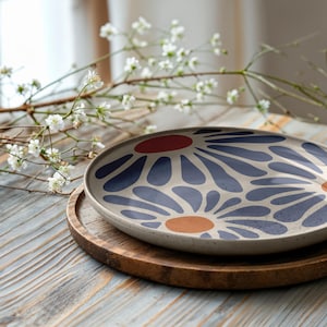 May include: A white ceramic plate with a blue and orange floral design. The plate is on a wooden coaster.