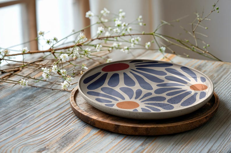 May include: A white ceramic plate with a blue and orange floral design. The plate is on a wooden coaster.