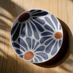 May include: A white ceramic bowl with a blue and orange floral pattern. The bowl has a round shape and a smooth, glossy finish.