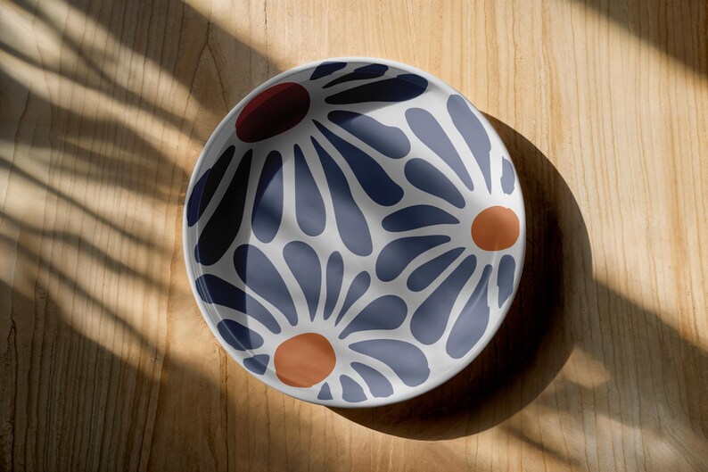 May include: A white ceramic bowl with a blue and orange floral pattern. The bowl has a round shape and a smooth, glossy finish.