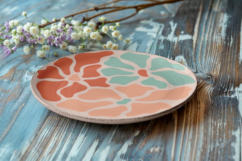 Puede incluir: Un plato decorativo de cer&aacute;mica con un dise&ntilde;o floral en tonos coral y turquesa. El plato se encuentra sobre una superficie de madera envejecida, te&ntilde;ida de azul, con una ramita de flores en el fondo.
