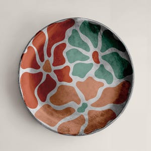 Puede incluir: Plato redondo decorativo con un dise&ntilde;o floral. El plato presenta un borde gris oscuro y un dise&ntilde;o de formas rojas, naranjas y verdes separadas por l&iacute;neas plateadas. Se encuentra sobre un fondo neutro.