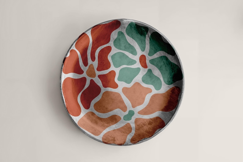 Puede incluir: Plato redondo decorativo con un dise&ntilde;o floral. El plato presenta un borde gris oscuro y un dise&ntilde;o de formas rojas, naranjas y verdes separadas por l&iacute;neas plateadas. Se encuentra sobre un fondo neutro.