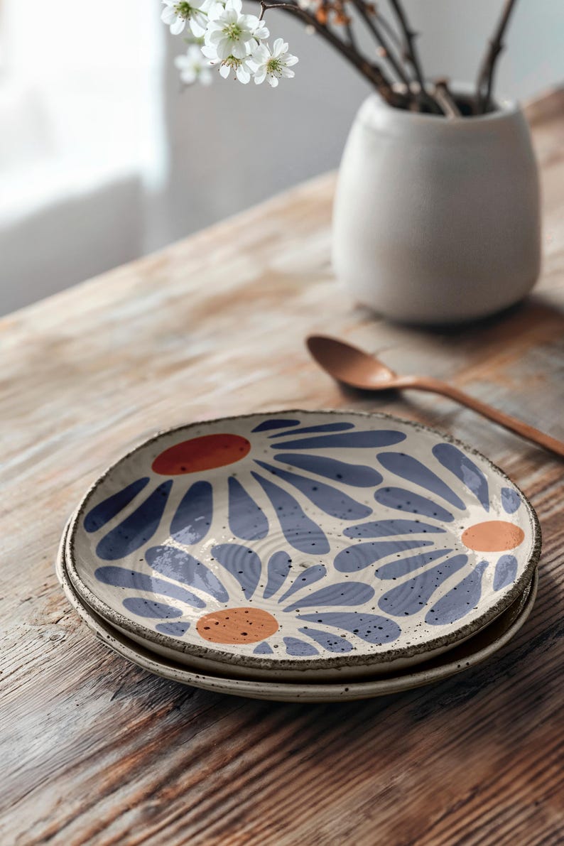 May include: A set of two ceramic plates with a white background and a blue and orange floral pattern. The plates are stacked on top of each other on a wooden table.