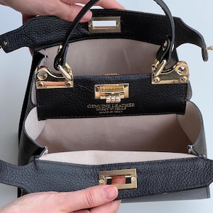 K&ouml;nnte beinhalten: Schwarze Ledertasche mit goldenen Beschl&auml;gen und zwei separaten F&auml;chern. Die Tasche ist ge&ouml;ffnet und das Innere ist mit einem hellbeigen Stoff ausgekleidet. Das Etikett lautet "Echtleder, Borse in Pelle, Hergestellt in Italien."
