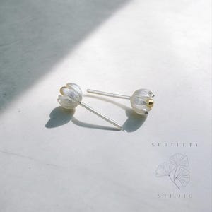 May include: A pair of silver flower stud earrings with a gold center. The earrings are delicate and feminine.