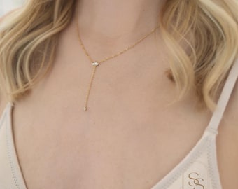 May include: A gold chain necklace with a small cluster of clear stones at the center and a single clear stone dangling from the bottom.