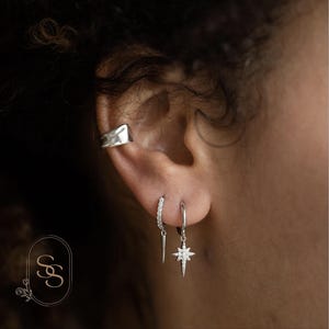 Könnte beinhalten: Silberner Ohrclip, Creolen und ein sternförmiger Ohrhänger mit Zirkonia-Steinen.