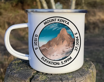 May include: White enamel camping mug with a black and white graphic of Mount Kenya. The graphic includes the mountain's coordinates and elevation: 0.1521° S, 37.3084° E, Elevation: 5,199M.
