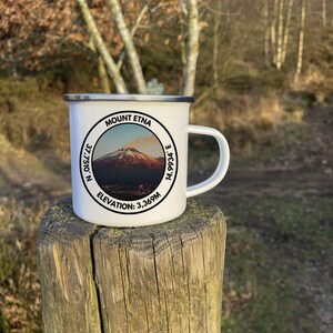 A 350ml White Enamel Mug with a circular logo displaying Mount Etna and the official coordinates and elevation. On the side of the mug is a Italian flag to show where the summit lies internationally!