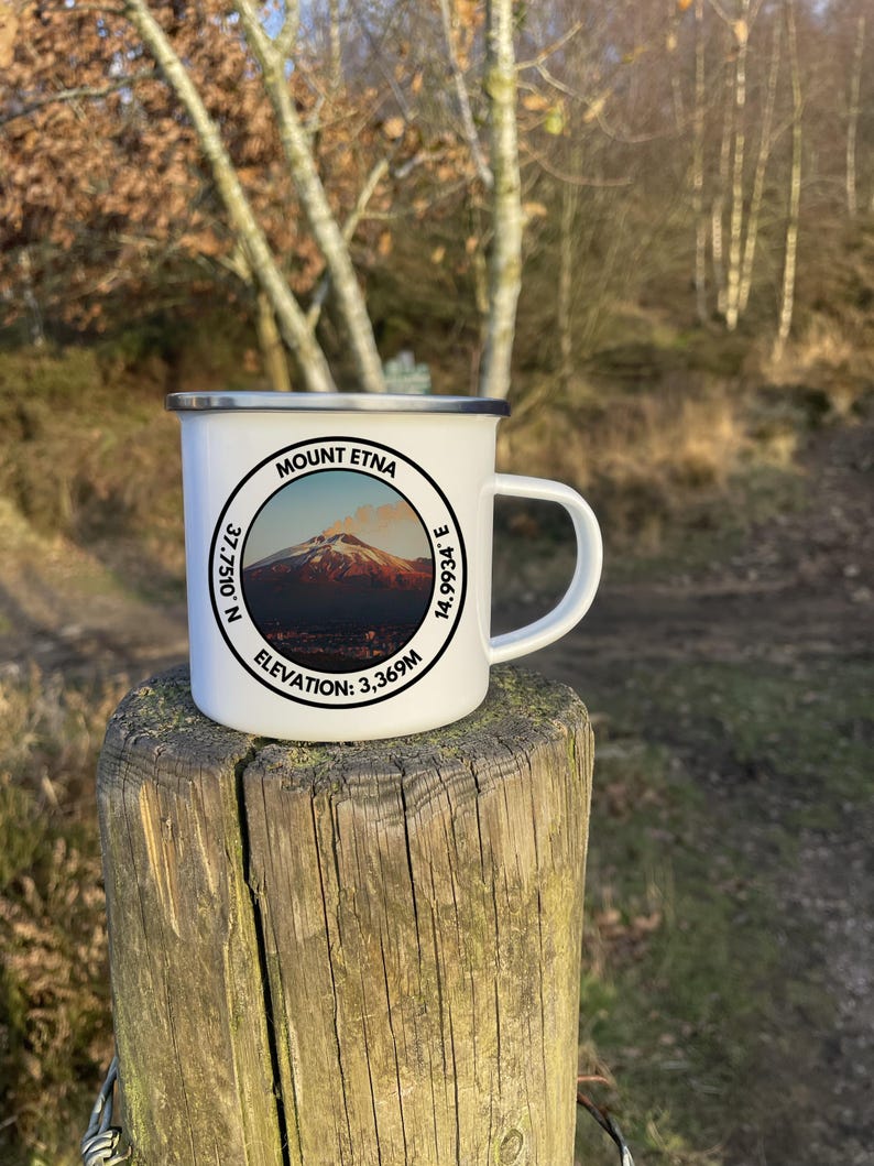A 350ml White Enamel Mug with a circular logo displaying Mount Etna and the official coordinates and elevation. On the side of the mug is a Italian flag to show where the summit lies internationally!