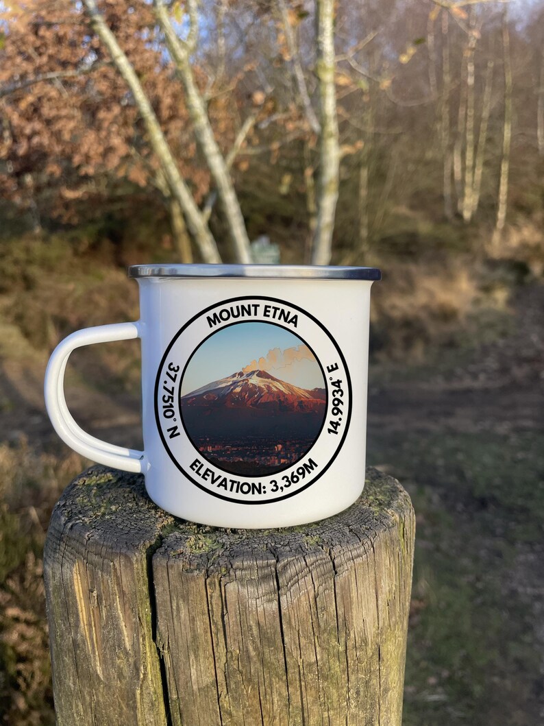 A 350ml White Enamel Mug with a circular logo displaying Mount Etna and the official coordinates and elevation. On the side of the mug is a Italian flag to show where the summit lies internationally!