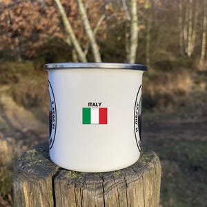 A 350ml White Enamel Mug with a circular logo displaying Mount Etna and the official coordinates and elevation. On the side of the mug is a Italian flag to show where the summit lies internationally!