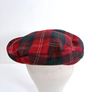 May include: A red, green, and white plaid flat cap. The cap is made of a soft material and has a rounded crown and a small, stiff brim. The plaid pattern is a classic design, with intersecting lines of red, green, and white.