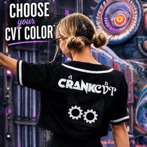 May include: Black crop top with white trim and the text "CRANKCØT" in white. A cat face with gear-shaped eyes is printed below the text. The top has short sleeves with white stripes. The words "CHOOSE your CVT COLOR" are at the top.