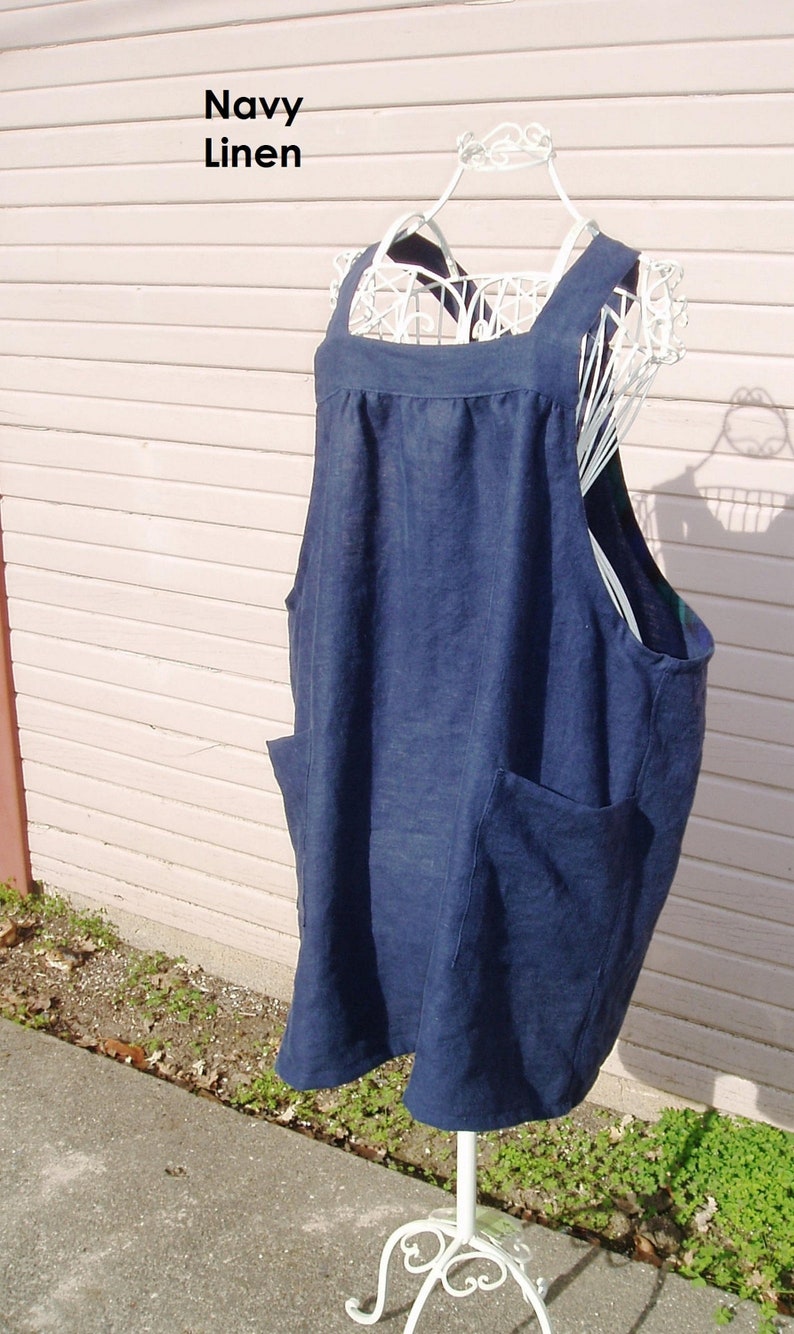 May include: Navy linen apron with two large pockets. The apron is hanging on a white metal stand.