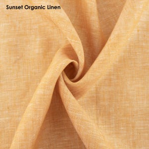 May include: Close-up of a textured, organic linen fabric in a warm sunset orange color. The fabric is folded and draped, showcasing its soft and natural texture.