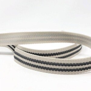 May include: Two pieces of off-white webbing with black stripes. The webbing is woven and has a textured surface.