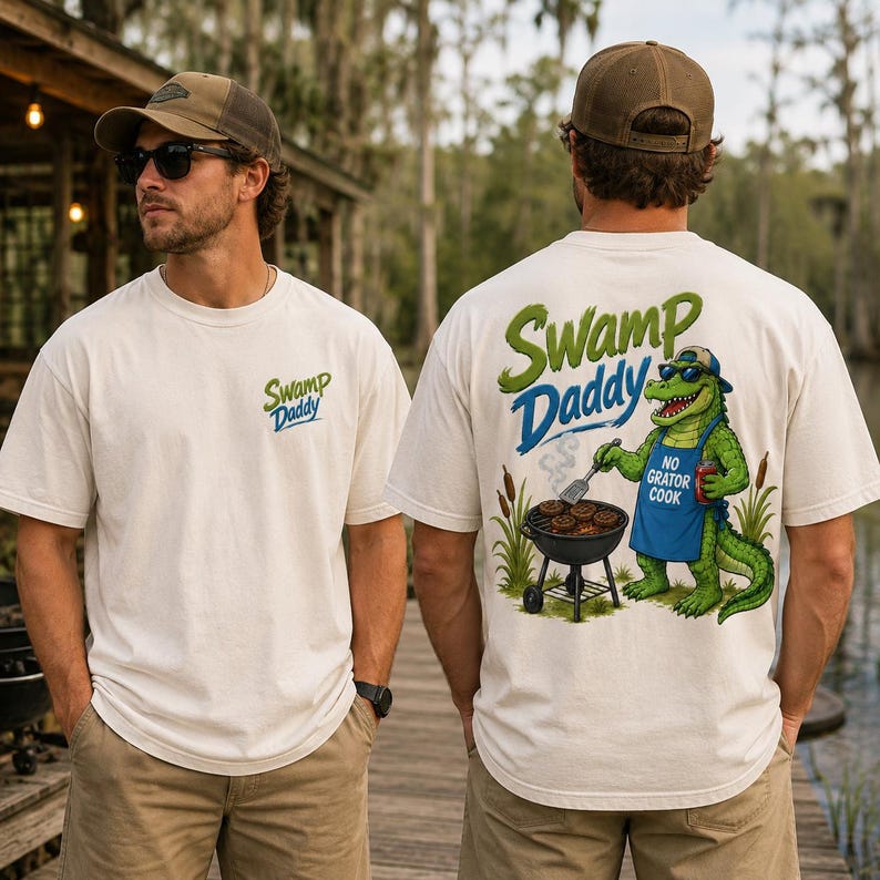 May include: Off-white t-shirts with the text "Swamp Daddy" in green and blue. One shirt has the text on the front, and the other has a cartoon alligator grilling burgers on the back, with the text "No Gator Cook".