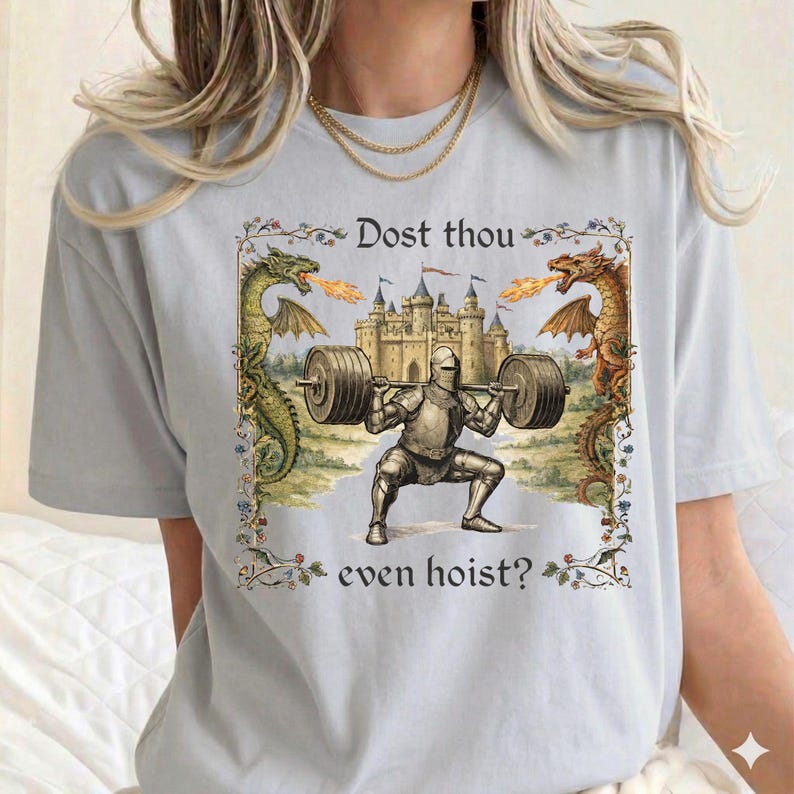 May include: Light blue t-shirt featuring a medieval knight squatting with a barbell, with a castle in the background. The shirt has the text "Dost thou even hoist?" with dragons on either side.