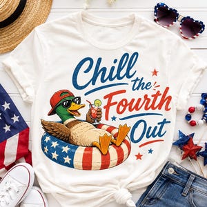 Pode incluir: Camiseta branca com um desenho de um pato com óculos de sol e boné vermelho, relaxando em um flutuador patriótico com um coquetel. O texto diz "Chill the Fourth Out" em vermelho e azul.
