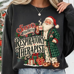 May include: A charcoal gray sweatshirt featuring a graphic of Santa Claus in a green plaid robe and pajamas, holding a mug with lung illustrations. The text reads Santa's Favorite Respiratory Therapist, surrounded by gift boxes and snowflakes.