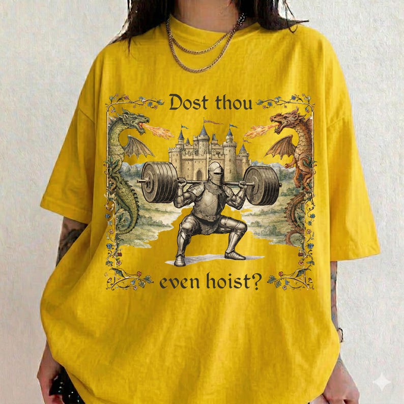 May include: Mustard yellow t-shirt featuring a medieval knight lifting weights with a castle backdrop and dragons. The text reads "Dost thou even hoist?" in a decorative font. The design is framed with floral elements.