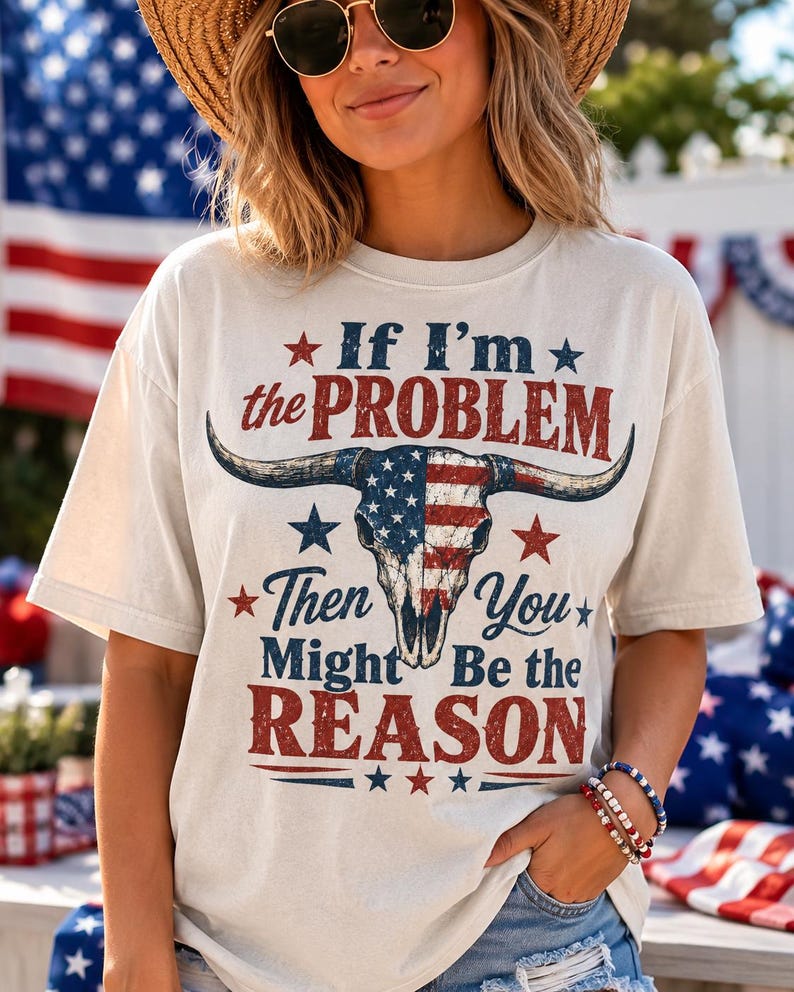 May include: Cream-colored t-shirt with the text "If I'm the PROBLEM Then You Might Be the REASON" in red and blue. The graphic features a bull skull with an American flag design. The shirt is short-sleeved.