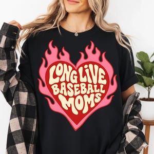 May include: Black t-shirt with a pink and red heart-shaped graphic. The graphic features the text "LONG LIVE BASEBALL MOMS" in a retro font, surrounded by flames. The shirt is a casual style.