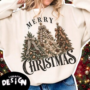 May include: A cream-colored long-sleeve sweatshirt featuring the text MERRY CHRISTMAS in black script. The design includes three stylized Christmas trees decorated with bows, ornaments, and pinecones, with one tree featuring a buffalo plaid pattern.