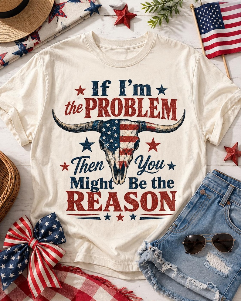 May include: Cream-colored t-shirt with the text "If I'm the PROBLEM Then You Might Be the REASON" and a bull skull design in red, white, and blue. The shirt is paired with denim shorts, sunglasses, and patriotic decorations.