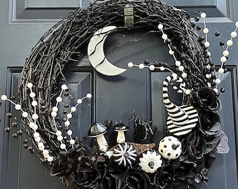 May include: A Halloween wreath with a black twig base, adorned with black roses, white beaded accents, and whimsical decorations. Features a crescent moon, striped horn, and mushroom accents. A festive, spooky home decor item.