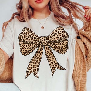 May include: A white t-shirt with a large brown and black leopard print bow design.
