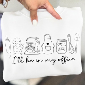 May include: White sweatshirt featuring a black line drawing of baking equipment: rolling pin, oven mitt, mixer, apron, flour jar, whisk, and spatula. The text "I'll be in my office" is below the drawing.