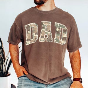 May include: A brown t-shirt with a camouflage print "DAD" graphic.