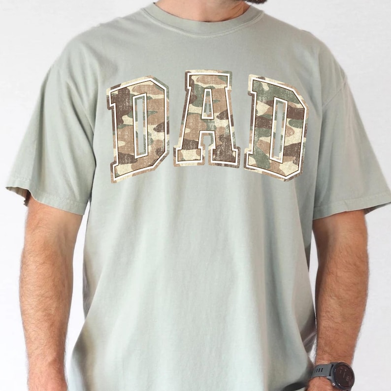 May include: A light green t-shirt with a camouflage print "DAD" graphic.