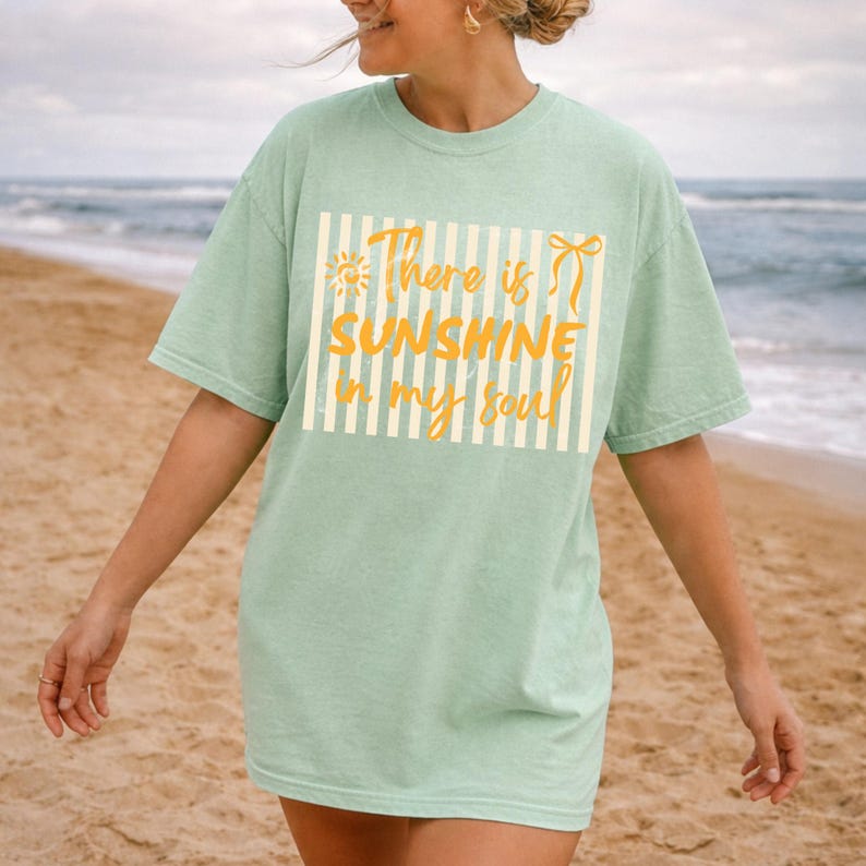 Puede incluir: Camiseta verde claro con el texto "There is sunshine in my soul" en amarillo. El texto est&aacute; dentro de un rect&aacute;ngulo blanco con rayas verticales. La camiseta tiene mangas cortas.