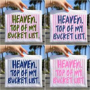 May include: Four white square towels with the text "HEAVEN. TOP OF MY BUCKET LIST." in different colors: green, blue, dark blue, and pink. Each towel has vertical stripes in a coordinating color.