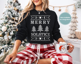 May include: Black sweatshirt with the text "MERRY SOLSTICE" in gray, with moon and tree designs. The person is wearing red and white plaid pajama pants and holding a mug with a Santa Claus design. A Christmas tree is in the background.