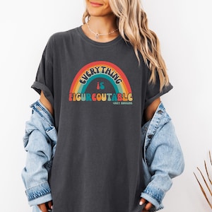 May include: Dark gray t-shirt with a rainbow graphic and the text "EVERYTHING IS FIGUREOUTABLE" in colorful retro font. The shirt has a relaxed fit and rolled sleeves, suggesting a casual style.