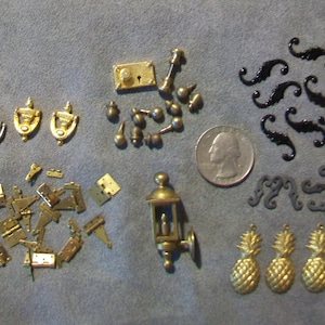 May include: An assortment of miniature hardware and decorative elements in gold and silver tones. Includes door knockers, hinges, a lantern, pineapple charms, and decorative black flourishes. A US quarter provides scale.